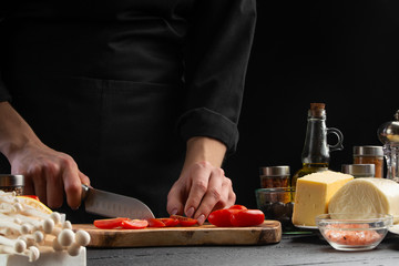 Cook on a wooden board slices cherry tomatoes, close-up, macro. Salad, organic ingredients and products. Vegetarian and tasty food.