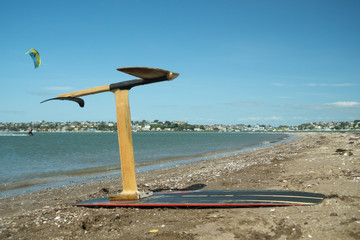 A home made 3d printed kite hydrofoil on a beach while a man kitesurfs in the background.