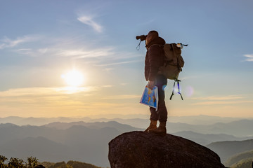 Young man with backpack enjoying sunset on binoculars peak of mountain layers line.Travel hiking.