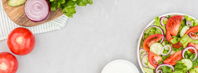 Healthy vegetarian dish on table, vegetable salad with fresh tomato, cucumber, lettuce, red onion on gray concrete background. Diet menu. Top view. Flat lay, mockup, template with copy space
