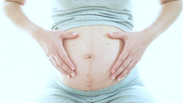 Pregnant woman holding her hands in a heart shape on her pregnant belly, white, closeup