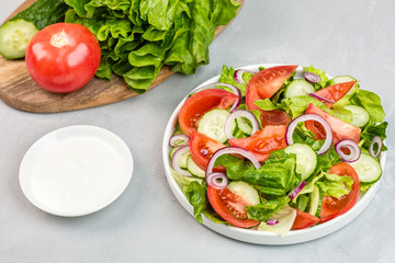 Healthy vegetarian dish on table, vegetable salad with fresh tomato, cucumber, lettuce, red onion on gray concrete background. Diet menu. mockup, template