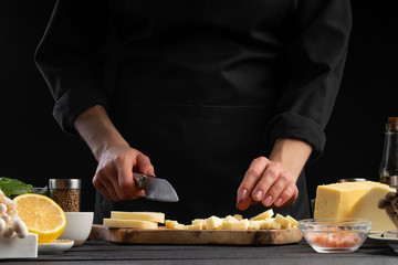 Chef slices mazzarella cheese to prepare a delicious and fresh salad. Vegetarian and fresh food, gastronomy and cooking, recipe book and recipes. On a black background