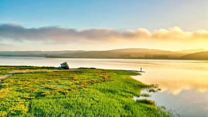A shipwreck and a man fishing at sunrise