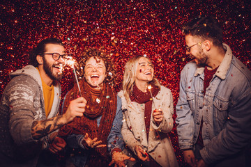Group of happy friends celebrating New Year with sparklers and confetti. New year party.