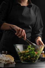Cooking Greek salad on a black background, vertical frame. Healthy and tasty food.