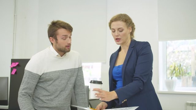 Woman with coffee and scheme in hands discuss project of houses with workmate