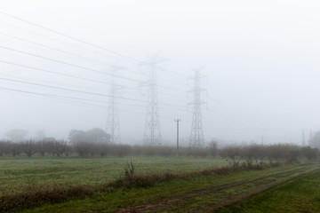 Foggy Landscape With High Voltage Poles Along Rural Road