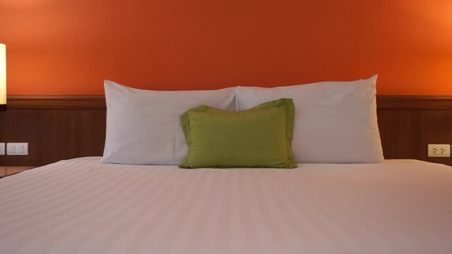 Hotel room interior with white clean bed with two white pillows and a green cusion in the middle, panning shot from left to right.