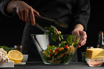 Cooking a salad, the cook prepares a salad on a dark background with ingredients. Delicious and healthy food.