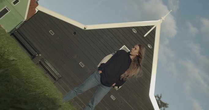 Woman posing wearing vlack hoodie in front of wooden dark Dutch house