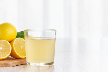 A glass of lemon juice and lemons on a table.