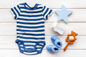Blue bodysuit for baby boy near children's accessories on white wooden background top-down