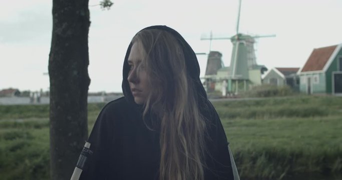 Young smiling fashion model woman girl wearing black hoodie posing in the street with channel and windmills on the  background