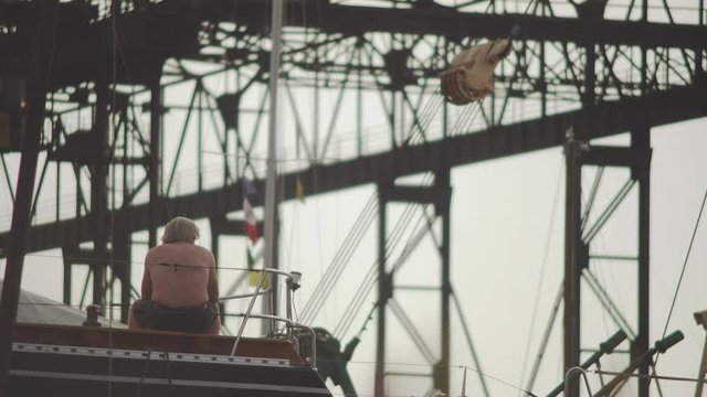Person sitting in his boat and contemplating in front of industrial port structures