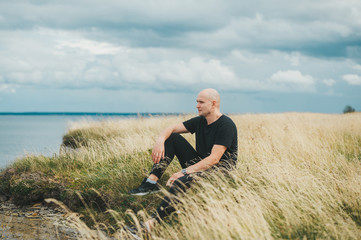 Naklejka na ściany i meble A man sitting on grass and admiring beauty of the coast.