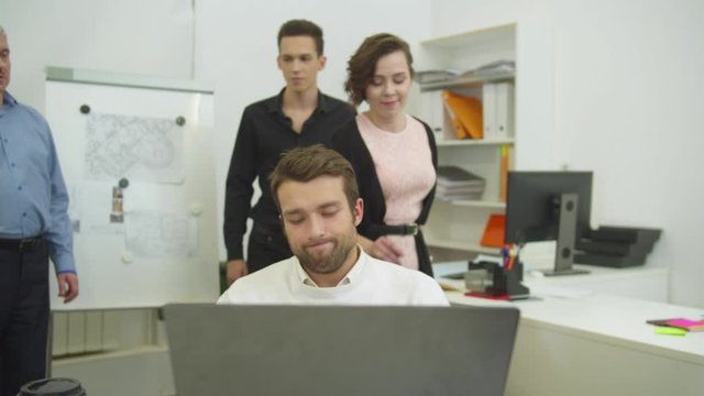 Young man works and colleagues live the office and slap him on the shoulder