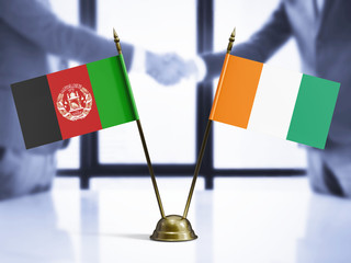 Cote D'Ivoire and Afghanistan mini table flags on white wooden desk. Diplomatic background with men...