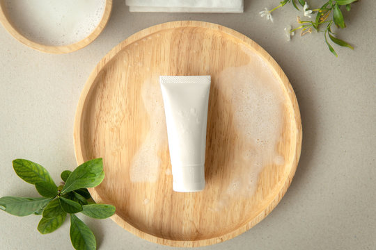 Top view of Organic gentle cleanser tube on a wooden plate decoration with leaves and white flower on grey background.