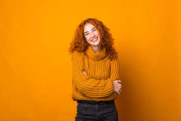 Photo of cute redhead girl, looking at camera with toothy smle, folded hands, sitting over orange...