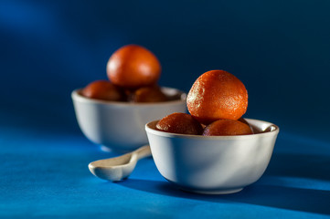 Indian Dessert : Gulab Jamun in bowl with spoon on blue background