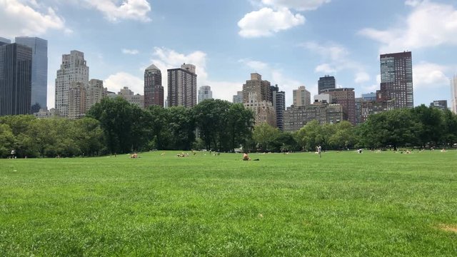 NEW YORK - JUNE 28, 2019: Crowded Central Park Sheep Meadow MANHATTAN public park. People sit, picnic, play games sports, talk, community, rest, relax, meditate, and play spikeball, grass, blue sky
