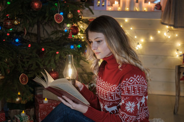 Young beautiful girl reading a book near the Christmas tree. Portrait of a girl on Christmas night.