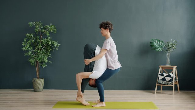 Male yoga teacher and female student are doing pair yoga in gym, girl is lifting guy talking discussing enjoyable activity. People and active lifestyle concept.