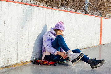 Lovely young woman sitting on ice ring and tieing shoelaces
