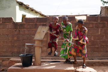 Three Little African Girls Having Fun While Pumping Water At The Borehole - obrazy, fototapety, plakaty