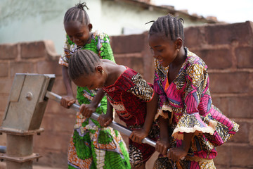Three Smiling Little African Girls Busy Fetching Water At The Village Pump - obrazy, fototapety, plakaty