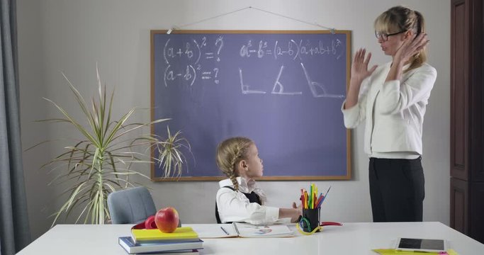 Tired Caucasian middle aged tutor holding head with hands and yelling as cute schoolgirl sitting at the table. Teacher tired of student's misbehavior. Private lesson, education. Cinema 4k ProRes HQ.