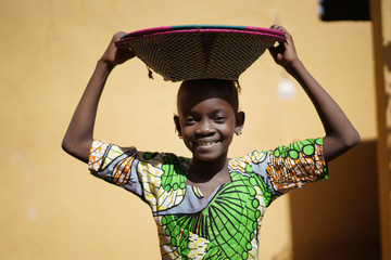 Cute African Girl Carrying a Couloured Handmade Straw Basket On Her Head