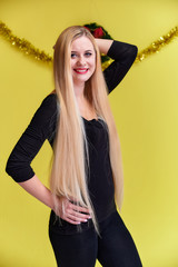 Concept of a young blonde woman with New Year's decor. Portrait of a cute girl in a black T-shirt with long beautiful hair and great makeup. Smiling, showing emotions on a yellow background.