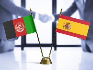 Spain and Afghanistan mini table flags on white wooden desk. Diplomatic background with men shaking...
