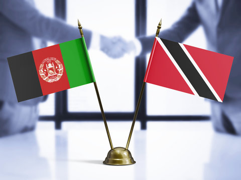 Trinidad And Tobago and Afghanistan mini table flags on white wooden desk. Diplomatic background with men shaking hands, international relations and agreements. - Powered by Adobe