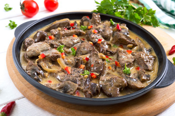 Turkey liver with onions and mushrooms in a creamy sauce on a white wooden background. Diet menu