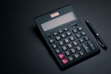 Top view on black accounting calculator and pen on a dark wooden office desk with copy space. Profit analysis, calculation of taxes and payments concept