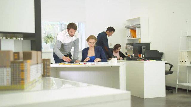 Engineers work with schemes of houses, colleague talk to woman 
