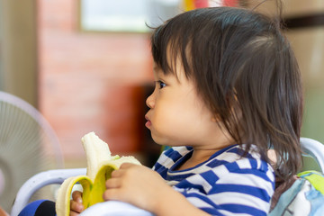Portrait image of baby 1-2 years old. Happy Asian child girl enjoy eating a banana with sweet smiling. Food and healthy kids concept.
