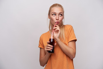 Pleasant looking young positive long haired blonde woman with casual hairstyle drinking soda with...