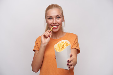 Joyful beautiful young lady with long blonde hair looking happily at camera and smling widely while...