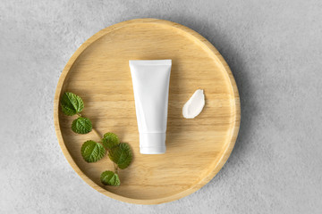 Top view of Organic gentle skincare tube with mint leaves and rich moisture butter cream smear on a wooden plate grey color as a background - obrazy, fototapety, plakaty