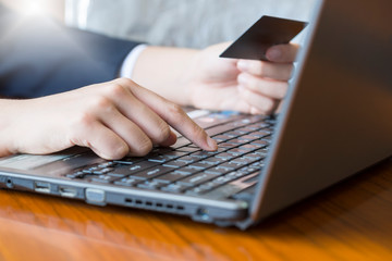 Features holding a credit card and using a laptop for online shopping.