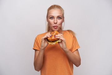 Indoor photo of attractive young hungry blonde lady with ponytail hairstyle chewing delicious...