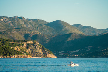 Motor boat is passing by a mountainous seashore with resort village in the valley