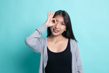 Beautiful young Asian woman show OK sign over her eye.