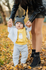 little baby boy learns to take first steps holding mom's hands in autumn