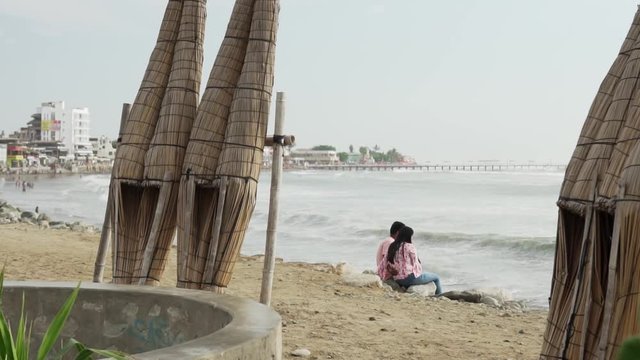 Slow Motion 120fps - Cute couple sitting on beach surrounded by caballitos de totora which decorate the entire coastline of Huanchaco in Peru