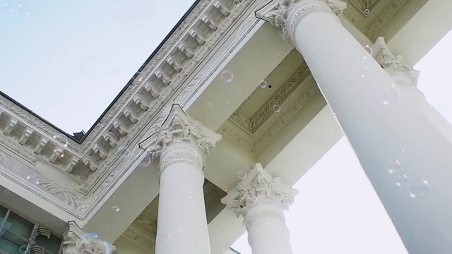 Many soap bubbles fly on the background of the classical portico with columns, constancy and variability, concept